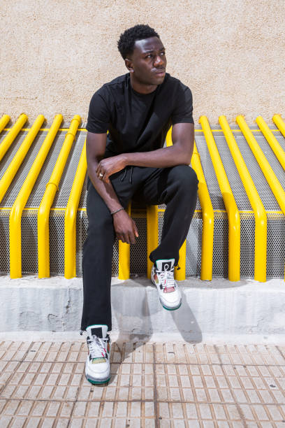 istock Pensive trendy ethnic guy looking away while sitting on street 1385379974