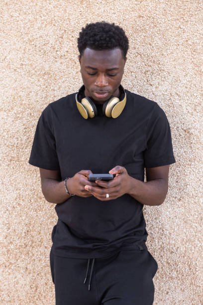 路上でベージュの壁の近くでスマートフォンを使用している深刻な黒人男性 - surfing wireless vertical outdoors lifestyles ストックフォトと画像