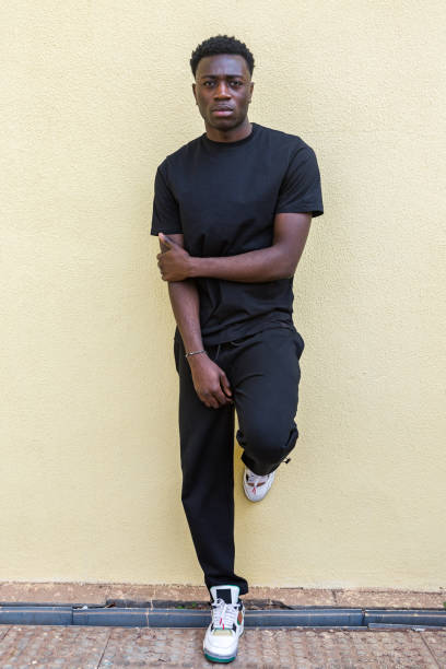 istock Serious black male standing on pavement near wall and looking at camera 1385379994