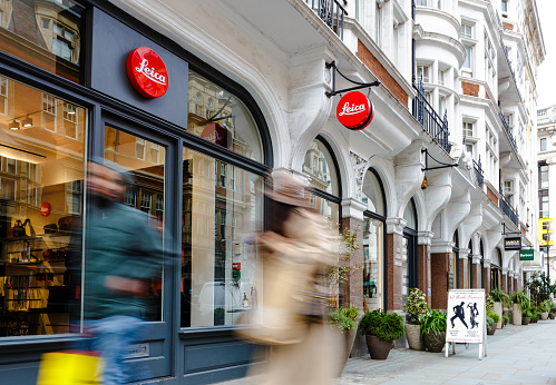London, UK - 14 March, 2022: color image depicting blurred motion of people walking past the exterior of a Leica camera store in central London, UK.