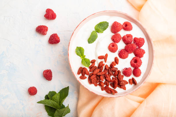 joghurt mit himbeeren und goji-beeren in keramikschüssel auf weißem betonhintergrund. draufsicht. - goji stock-fotos und bilder