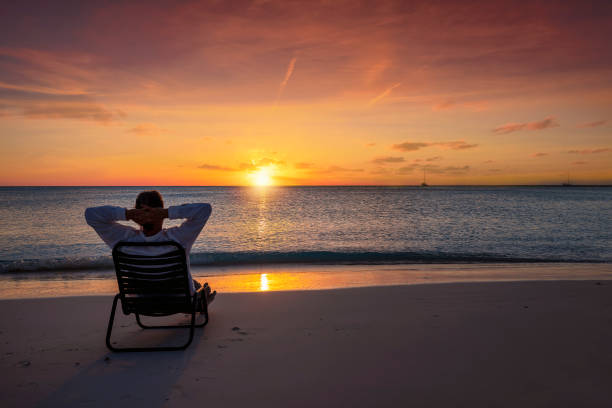 A man on vacation relaxes in a chair on a beach during sunset