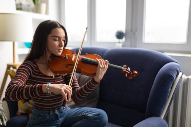 istock While sitting on her comfortable sofa, the female violinist practices playing the violin. 1385391558