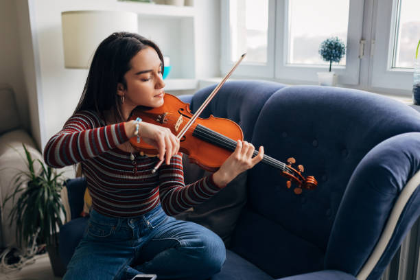 istock While sitting on a comfortable sofa by the window, a talented young violinist plays the violin. 1385392283