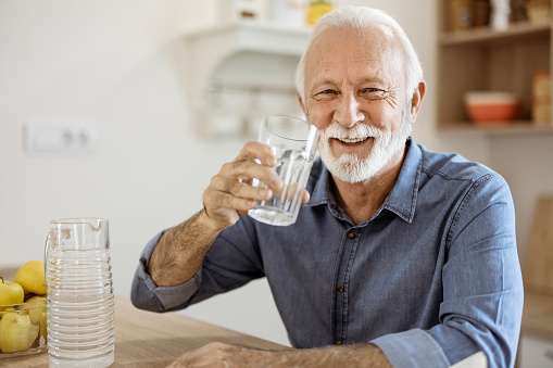Senior man drinking a glass of water with a happy face and looking at camera