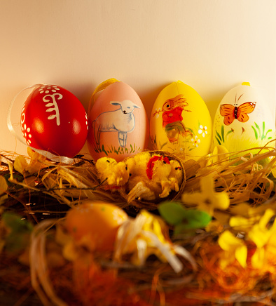 Four different colored Easter eggs with animals are placed on a decorated wreath. There is a rabbit, a lamb and a butterfly.