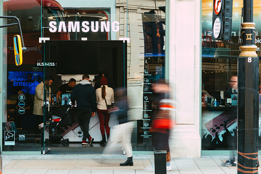 London, UK - 14 March, 2022: wide angle image depicting the exterior of a Samsung electronics store in central London, with blurred motion of people walking past on the street outside the shop.