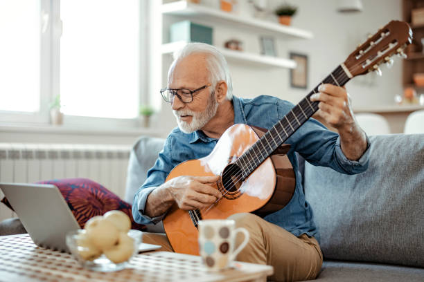 istock Senior Man Watching Video on Laptop while Learning to Play Guitar 1385394579