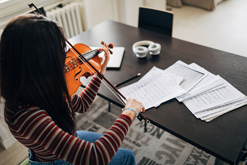 The female violinist sits at a table, surrounded by notes, and practices playing the violin.