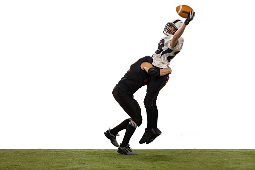 Jumping with ball. Two male american football players playing during sport match on grass flooring isolated on white background. Concept of sport, challenges, goals, strength. Poster, banner for ad