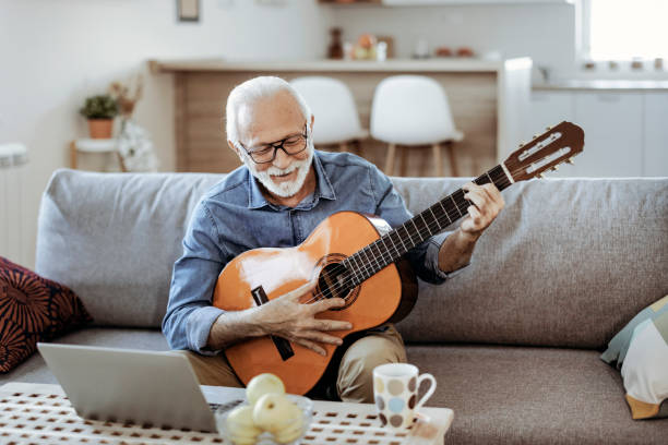 istock Senior Man Watching Video on Laptop while Learning to Play Guitar 1385398057