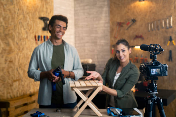 istock Two people in a carpentry workshop being filmed with a camera for a blog, showing how to make a chair. Focus is on camera. 1385398633