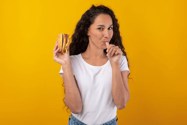 istock Happy Latin Lady Holding Burger Licking Finger At Studio 1385400462