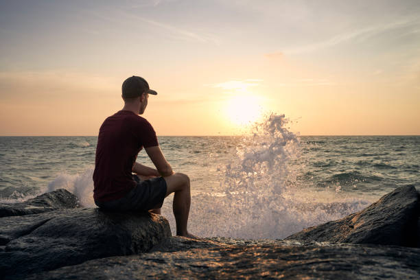 istock Man sitting on rock and watching sunset over ocean