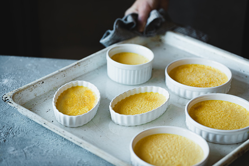 Close-up of six bowls of creme brulee in a white tray in kitchen.