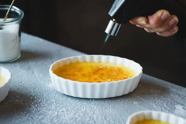 Close-up of a chef preparing creme brulee using blow torch. Caramelizing sugar over custard plate in kitchen counter.