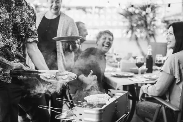 Chef cooking meat at barbecue family dinner outdoor in the backyard - Focus on left hand - Black and white edition