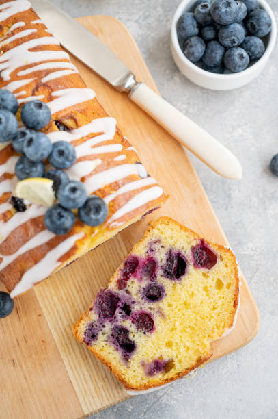 istock Lemon blueberry cake with lemon icing and fresh berries on top on the board on a gray concrete background with cup of tea. Selective focus. Copy space. 1385408766