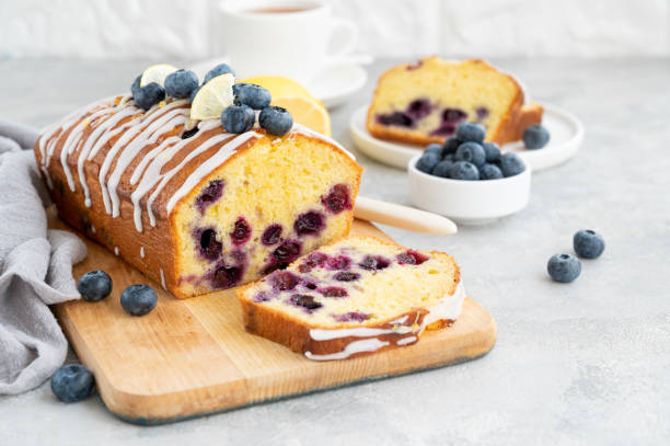 istock Lemon blueberry cake with lemon icing and fresh berries on top on the board on a gray concrete background with cup of tea. Selective focus. Copy space. 1385408768