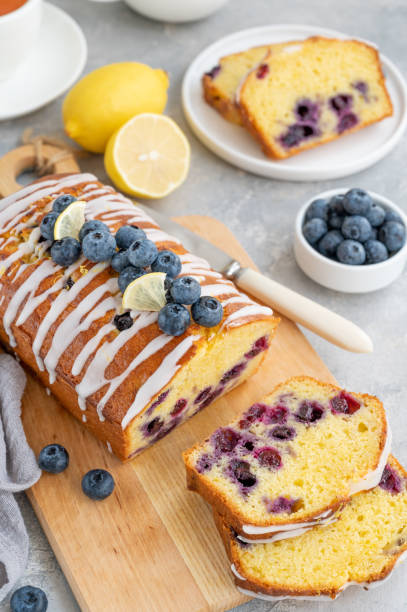 istock Lemon blueberry cake with lemon icing and fresh berries on top on the board on a gray concrete background with cup of tea. Selective focus. Copy space. 1385408769