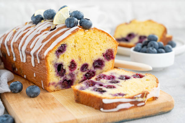 istock Lemon blueberry cake with lemon icing and fresh berries on top on the board on a gray concrete background with cup of tea. Selective focus. Copy space. 1385408770