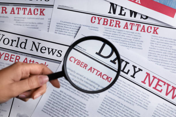 istock Woman using magnifying glass to read newspaper with headline CYBER ATTACK, top view 1385414988