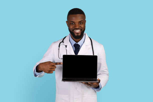 Handsome black doctor in white robe pointing at blank laptop screen
