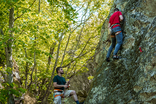 Two rock climbers looking down at a steep mountain with their climbing equipment