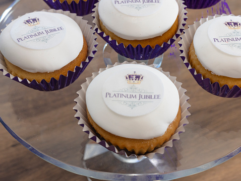 British Royal Jubilee Cupcakes, to celebrate the Queen's Platinum Jubilee.  Cupcakes with white fondant icing, with rice paper decorated with the words 'Platinum Jubilee' and an image of a purple and gold crown.