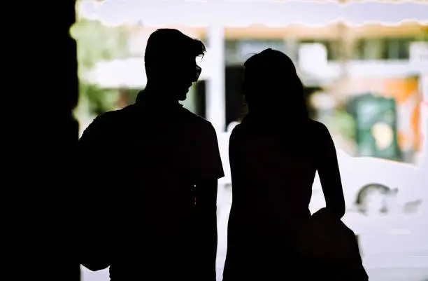 Photo of Silhouette of couple with shopping bags holding hands while walking on street