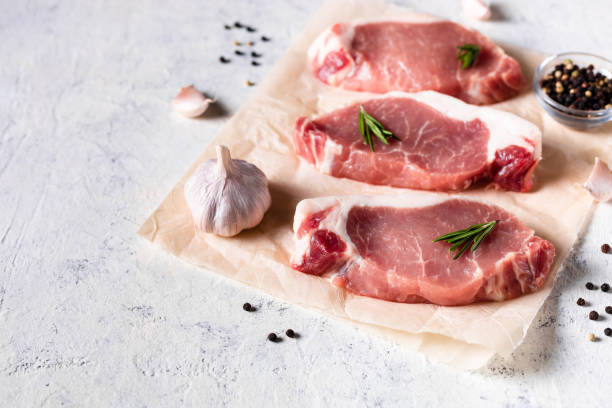 un trozo de cerdo fresco crudo con romero y ajo sobre un papel vax sobre fondo blanco. carne con especias - veal meat raw steak fotografías e imágenes de stock