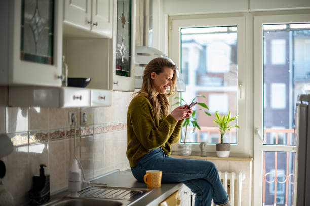 istock Woman standing in the kitchen and drinking cup of tea while using smartphone 1385428562