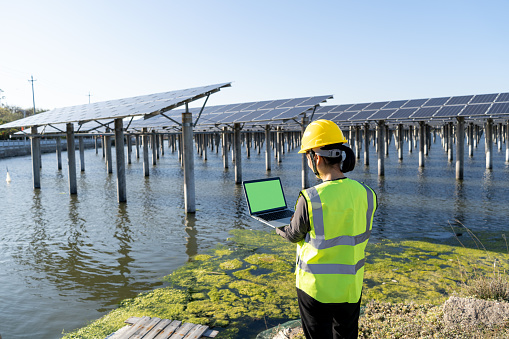 Back view of female engineer using laptop at solar power plant