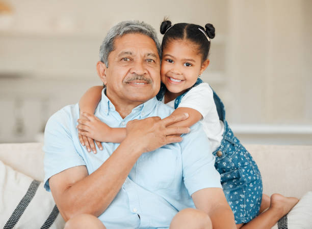 foto de un abuelo y una nieta uniéndose en el sofá de casa - grandparent adult smiling looking at camera fotografías e imágenes de stock