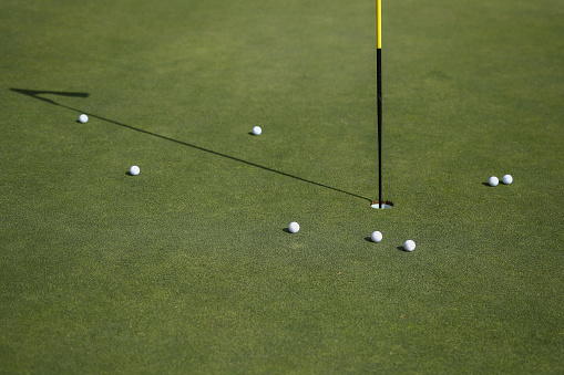A close up of golf balls around the pin on a green