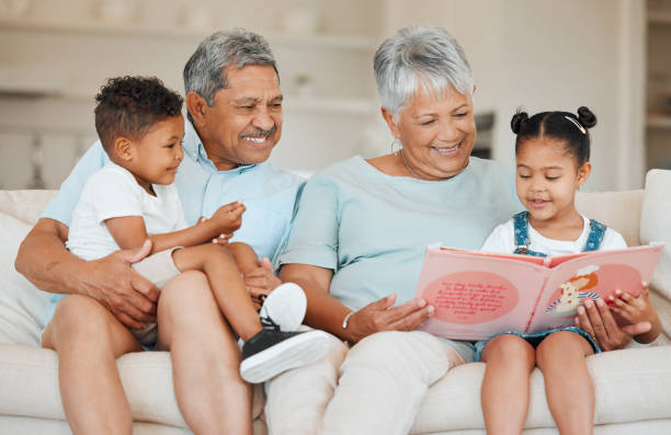 aufnahme von großeltern, die sich mit ihren enkelkindern auf einem sofa zu hause verbinden - grandparent family reading inside of stock-fotos und bilder