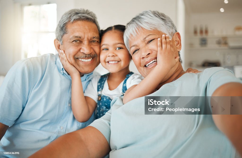Shot of grandparents bonding with their granddaughter on a sofa at home Being part of a family means smiling for photos Grandparent Stock Photo