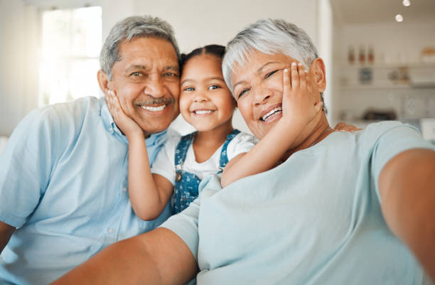 снимок бабушек  и дедушек, скрепляющихся со своей внучкой на диване дома - family стоковые фото и изображения