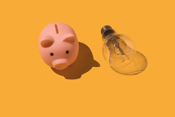 Piggy bank and light bulb on yellow background. Concept of electricity, rising prices, impoverishment and economy. stock photo