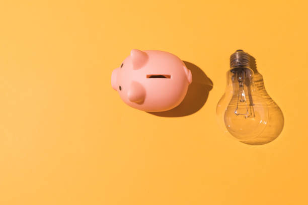 Piggy bank and light bulb on yellow background. Concept of electricity, rising prices, impoverishment and economy. stock photo