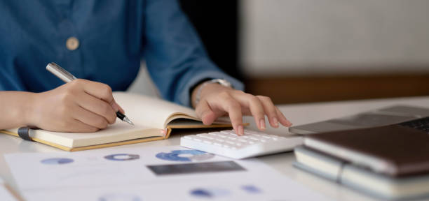 istock Close up woman using calculator working at office with reports document financial. 1385443303