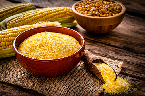 Close up view of a clay bowl filled with corn grits shot on rustic wooden table. Dried corn and corncobs complete the composition. High resolution 42Mp studio digital capture taken with Sony A7rII and Sony FE 90mm f2.8 macro G OSS lens