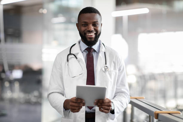 istock Positive young black doctor holding digital tablet, clinic interior 1385449823