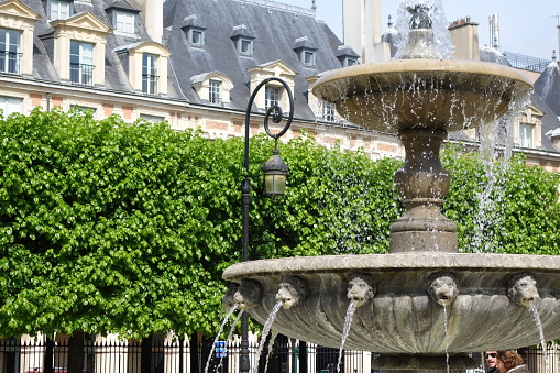 Spraying fountain at Place des Vosges with trees and building facade in the background