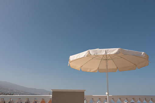 White beach  umbrella with a metal pole against a blue sky.