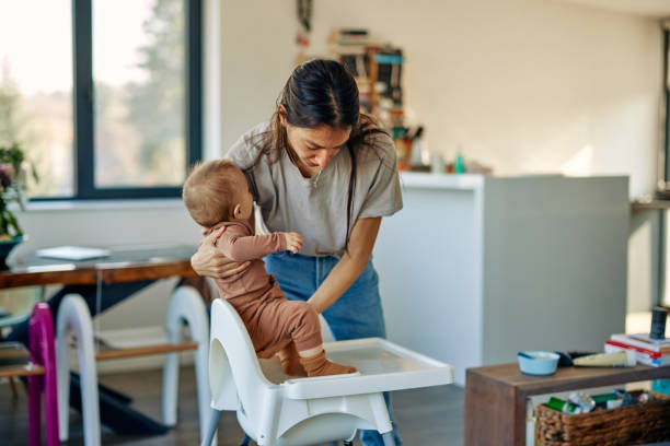 Mother putting her baby in high chair Its lunchtime. Mother putting her infant baby boy in high chair. Preparing him for lunch high chair stock pictures, royalty-free photos & images