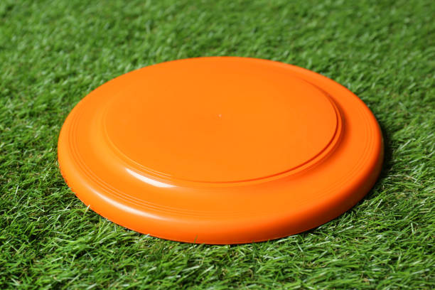 Orange plastic frisbee disk on green grass Orange plastic frisbee disk on green grass plastic disc stock pictures, royalty-free photos & images