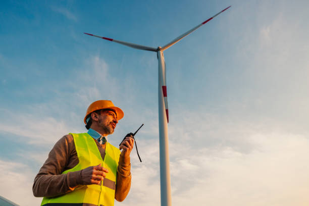 ingénieur debout sur le terrain avec des éoliennes utilisant un talkie-walkie - engineer wind turbine alternative energy energy photos et images de collection