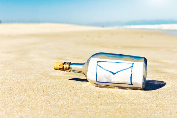 ボトル内のキャスタウェイのメッセージには、電子メールの封筒シンボルが含まれています - message in a bottle beached bottle desert island ストックフォトと画像