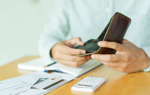 close up man hand opening empty wallet over calculator , debt expense bills monthly and credit card at the table in home office ,  managing payroll,money risk financial concept stock photo